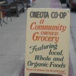 Signboard on a sidewalk says, "Oneota Co-op, a community owned grocery featuring local, whole and organic foods